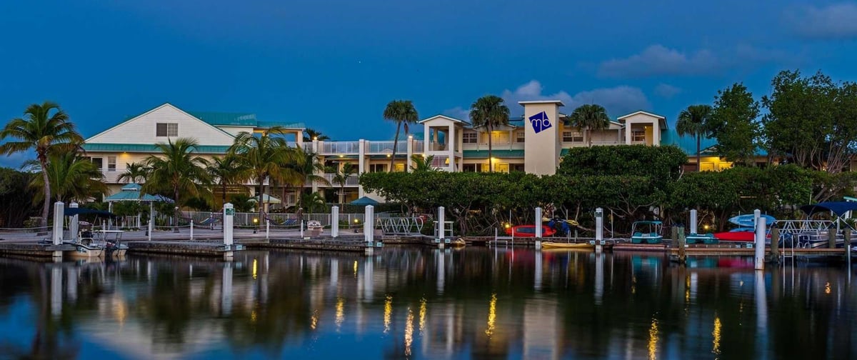 Dove Creek Resort & Marina entrance in daylight, low island-style buildings and palms along the arrival drive